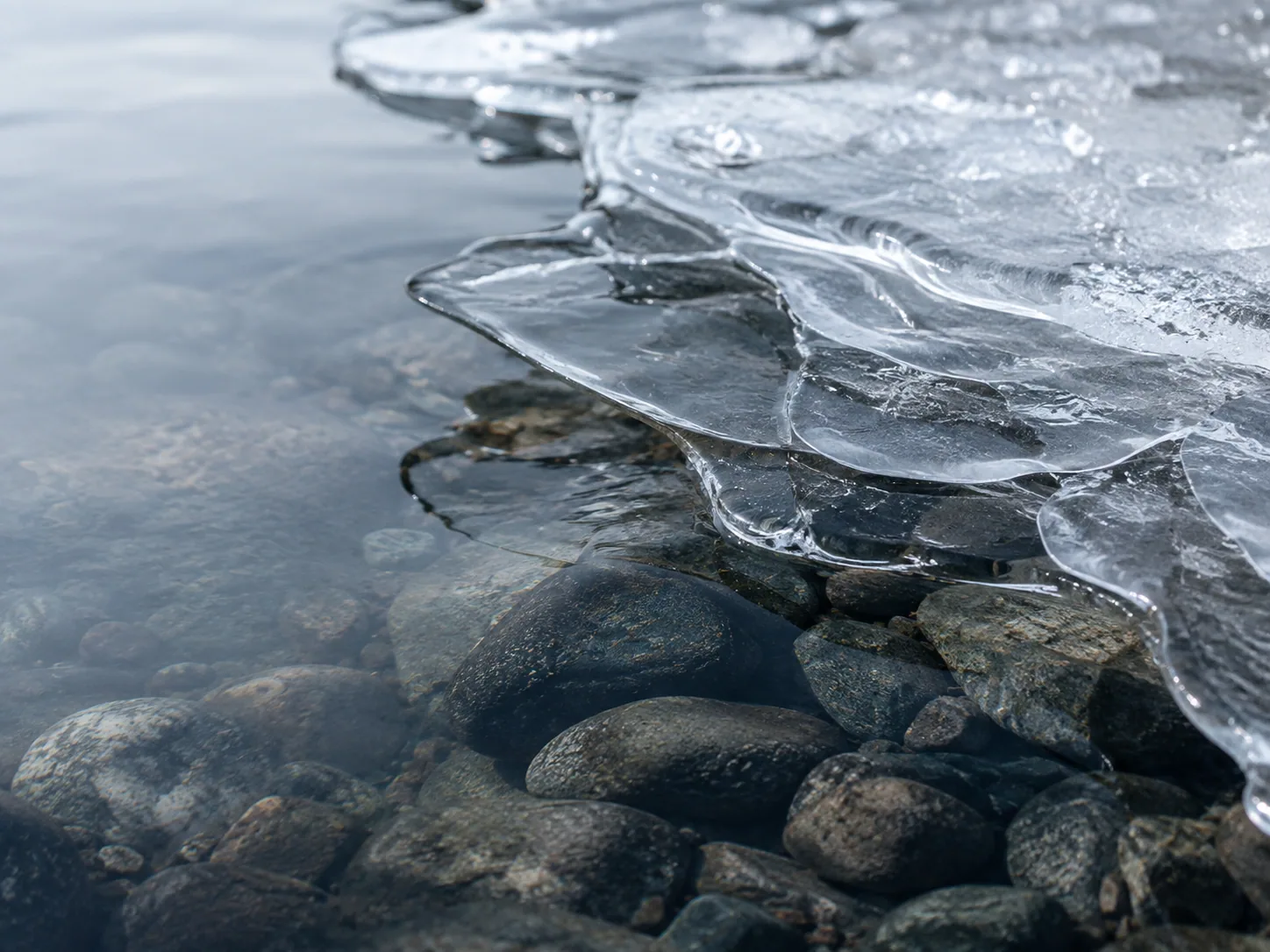 Layered ice, clear water and stones reveal the structure beneath the surface.